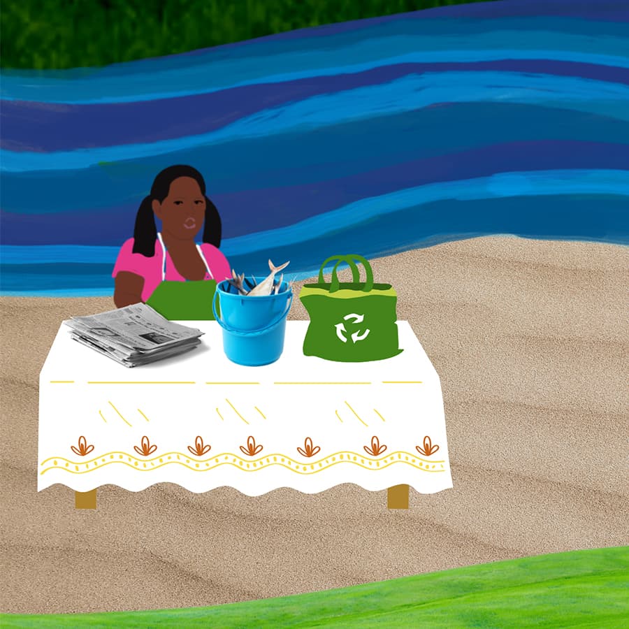 A fisherwoman sits behind her table on the sand next to a river. On the table is a bucket of fresh fish, a stack of newspapers for wrapping, and a reusable tote bag.